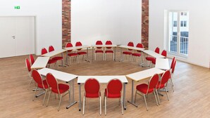 Une salle de conférence dotée d’une table ronde et de chaises rouges, de murs blancs et d’un mur en briques apparentes.