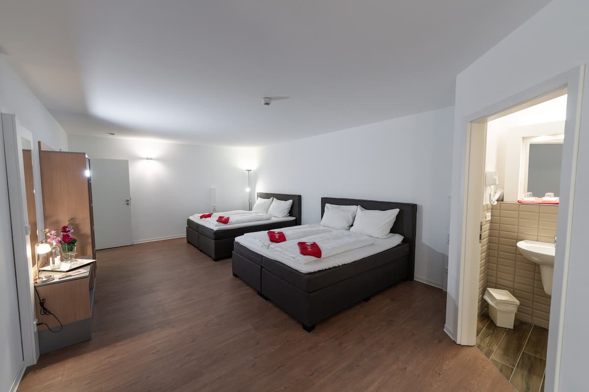 A hotel room with two beds, a desk with a lamp, and a bathroom with a sink and mirror.