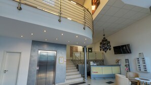 Un hall d’entrée moderne avec un escalier à volutes, un comptoir d’accueil, un lustre et un téléviseur à écran plat.