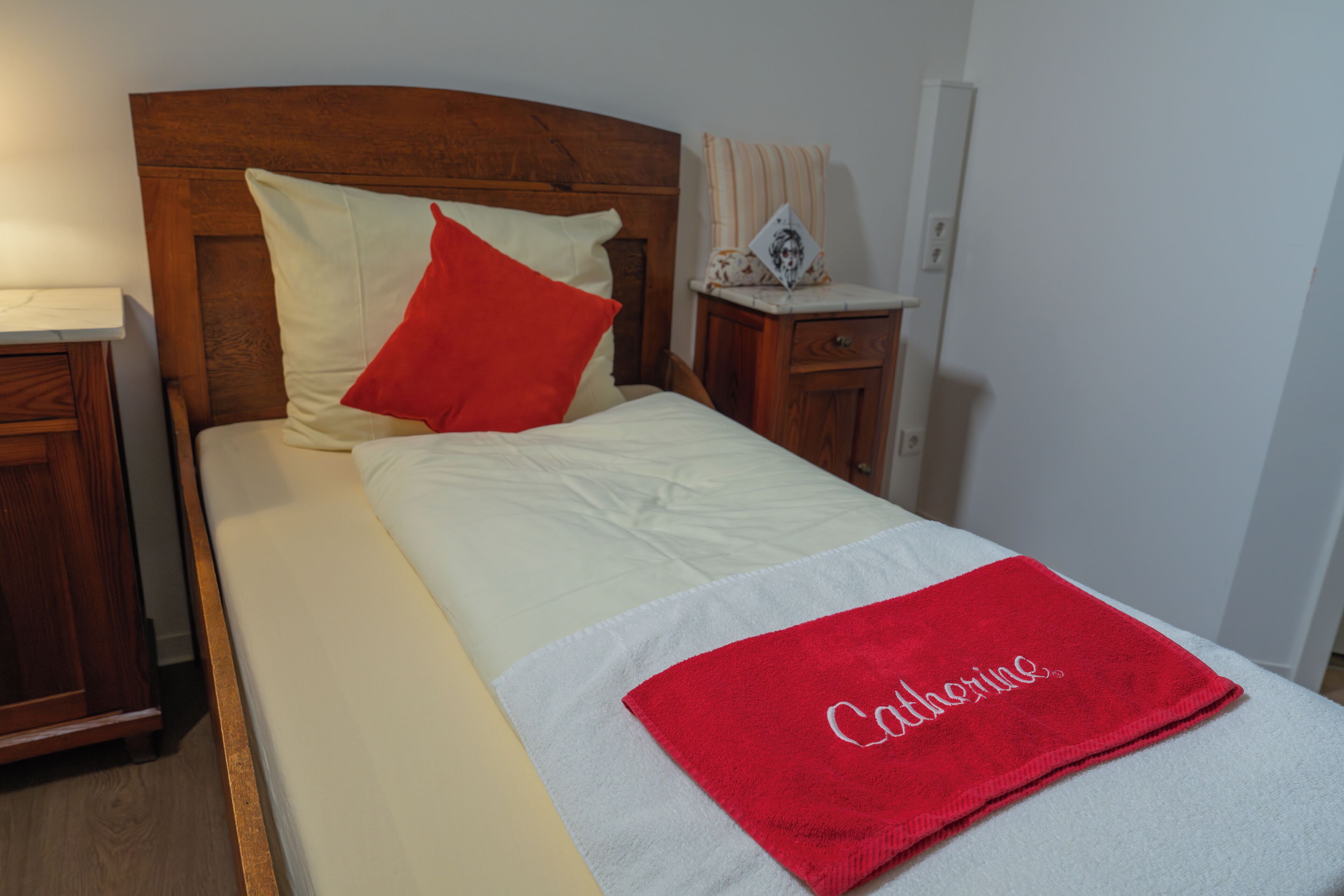 A neatly made bed with a red towel, a wooden headboard, and a bedside table with a lamp.