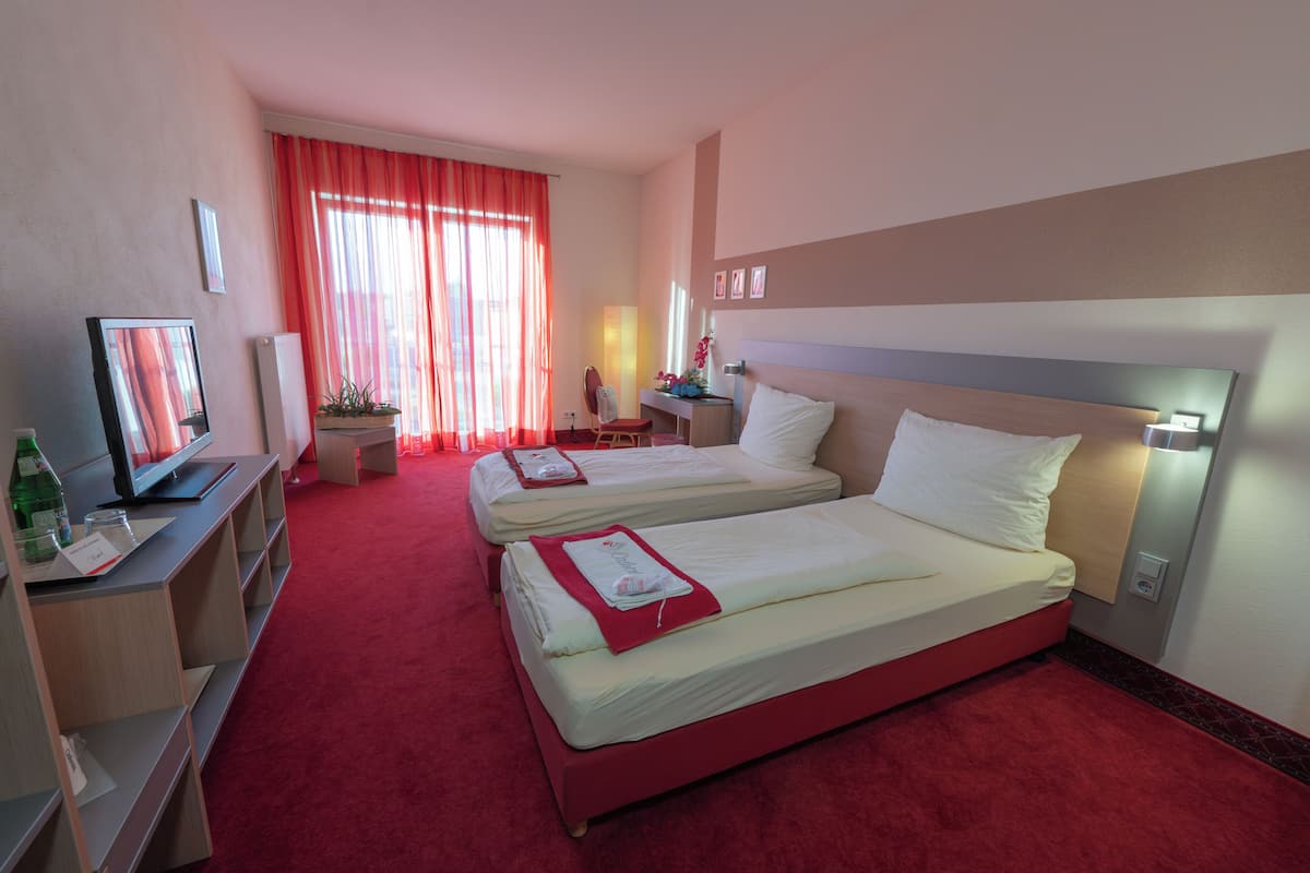 A hotel room with two beds, a desk, a television, and a window with curtains.