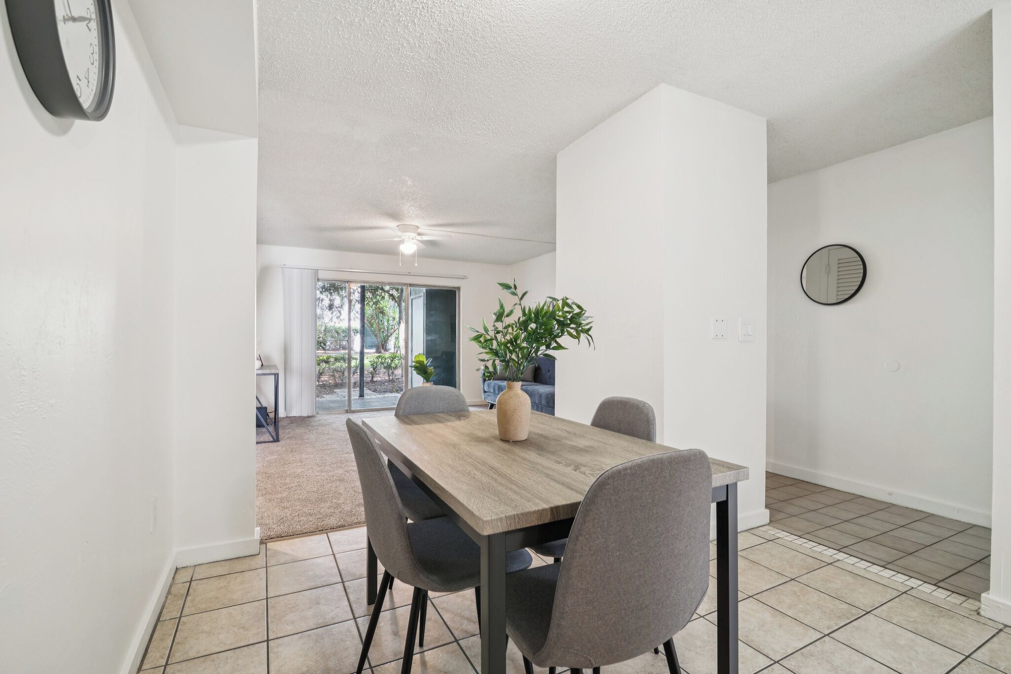 Un coin repas avec une table en bois, quatre chaises, un vase avec une plante et un ventilateur de plafond.