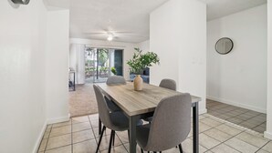 A dining area with a wooden table, four chairs, a vase with a plant, and a ceiling fan.