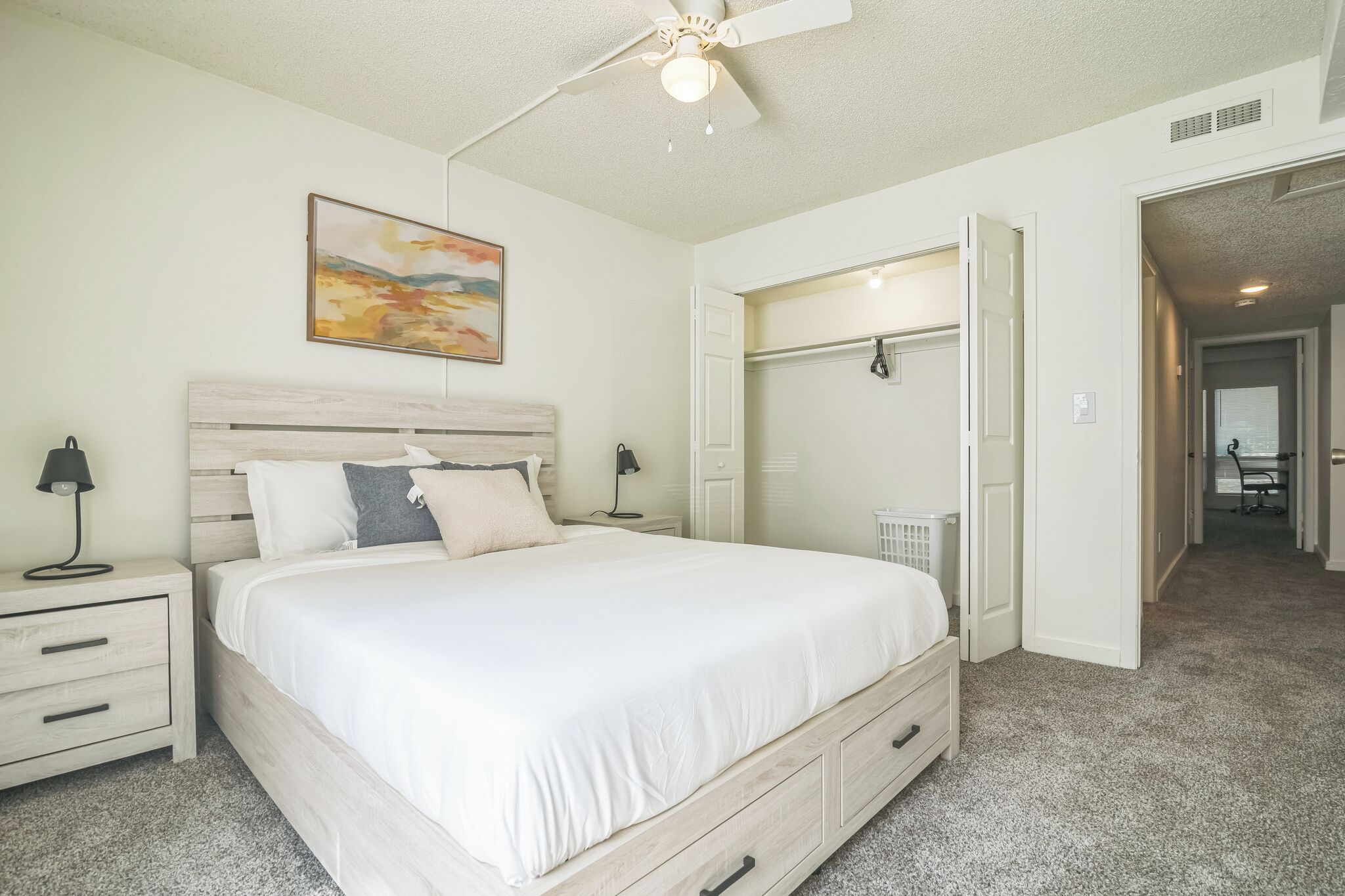 A bedroom with a bed, nightstands, a ceiling fan, a painting, and a walk-in closet.