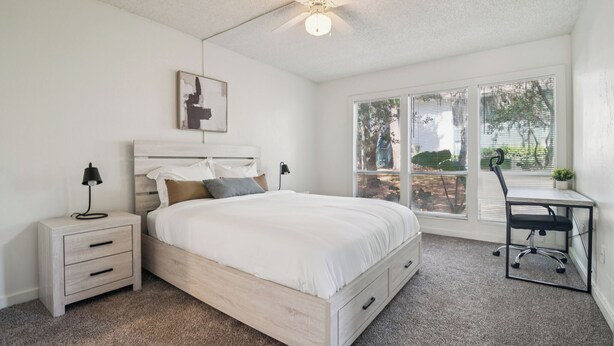 A bedroom with a bed, nightstands, a desk, and a ceiling fan.
