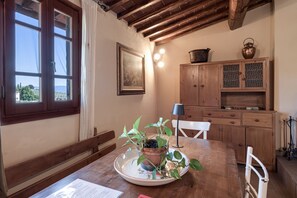 Un coin repas comprenant une table en bois, des chaises, une plante en pot, un tableau encadré et un meuble avec une lampe.