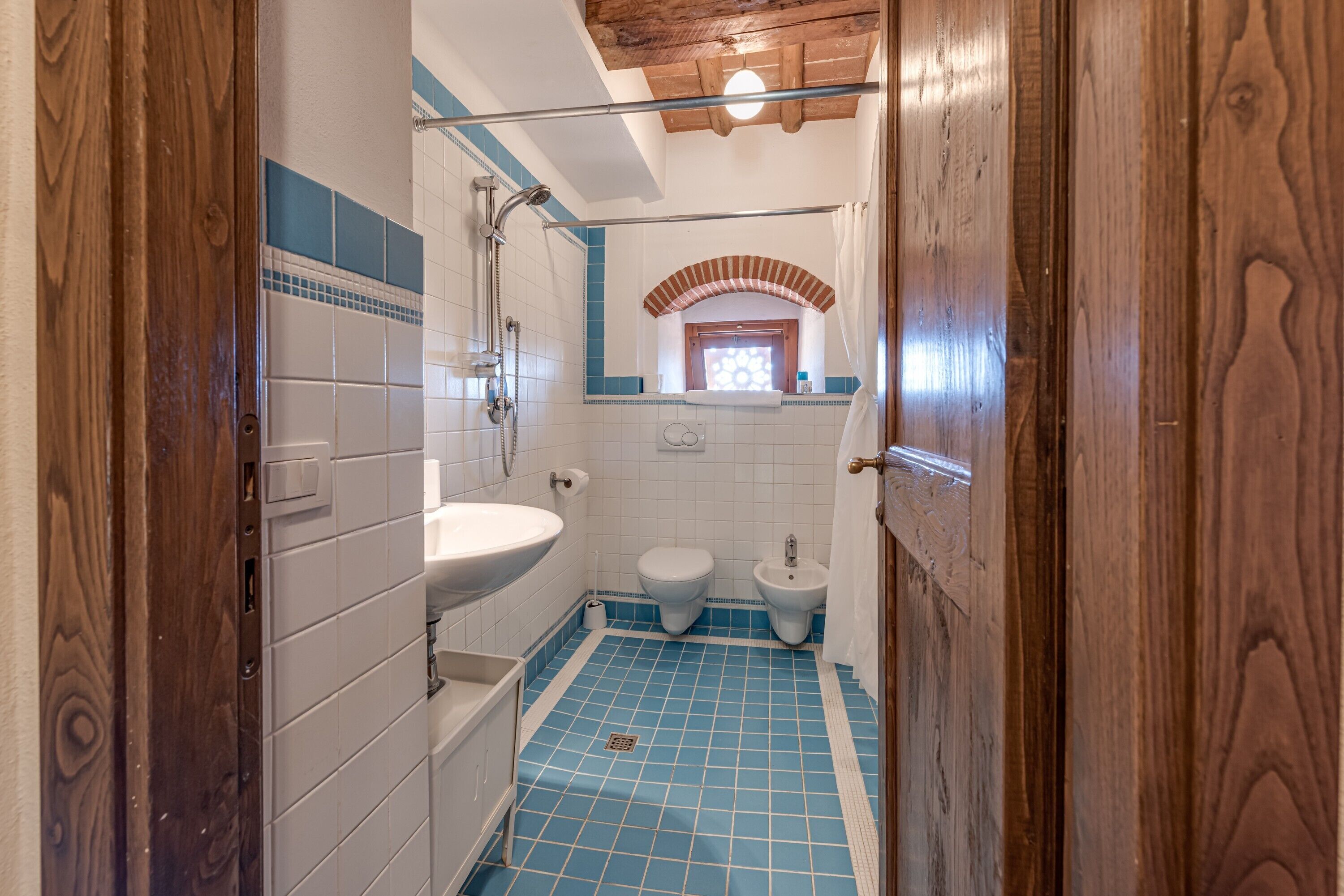 Une salle de bain équipée d’une douche, d’un lavabo, de toilettes, d’un bidet et d’un sol carrelé de carreaux bleus.