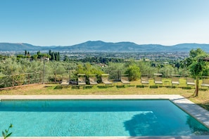 Une piscine rectangulaire, dotée de chaises longues et offrant une vue sur les montagnes lointaines.