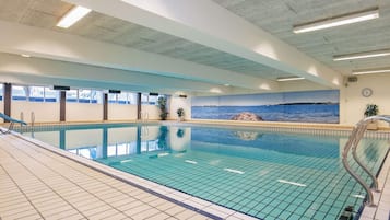 Una piscina interior con agua azul cristalina, paredes con azulejos y un mural de una escena costera.