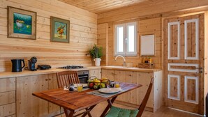 Een houten blokhut van binnen met een keuken, een eettafel, stoelen, een raam en een deur.