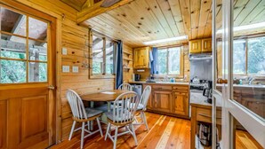Interior de una cabaña de madera con comedor, cocina y ventanas amplias.