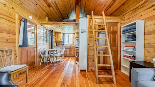 Interior de una cabaña de madera con comedor, cocina y una escalera que sube a un altillo.