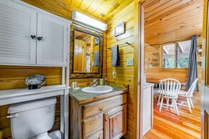 A wooden cabin bathroom with a sink, mirror, and white chairs.