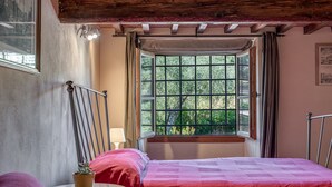 A bedroom with a bed, a window with curtains, a small table with a plant, and a lamp. - Studio 'Il Poderaccio Tramontana' with Shared Pool, Wi-Fi and Air Conditioning (Scandicci)