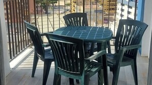 Un balcon avec une table et des chaises, une vue sur un terrain de sport et des bâtiments en arrière-plan.