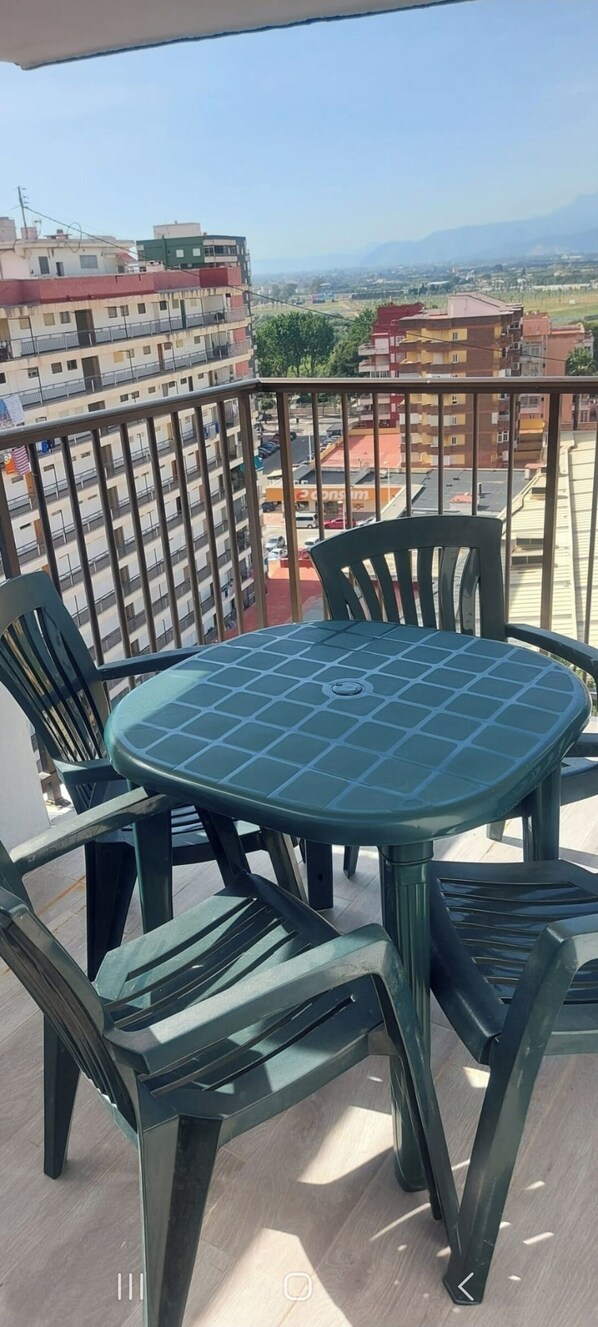Un balcon avec une table ronde et quatre chaises, d’où l’on peut admirer un panorama sur la ville, avec ses bâtiments et ses montagnes.