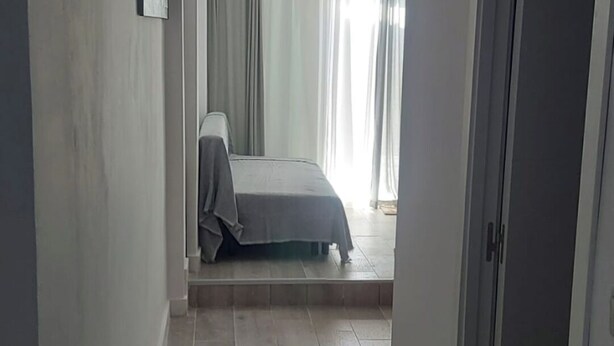 Un couloir étroit, avec un lit au fond, une porte sur la droite et un luminaire au plafond.