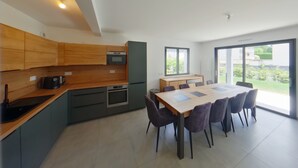 A modern kitchen with wooden cabinets, a built-in oven, and a dining area with a large table and chairs.