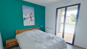 A bedroom with a large bed, a wooden headboard, a teal wall, and a painting of a ski scene.