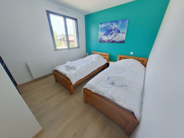 A room with two wooden beds, white bedding, a window, and a mountain painting on the wall. - Comfortable house in Les Rousses, 12 guests, near ski and lake (Les Rousses)