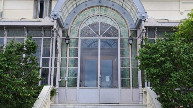 A building with a large arched entrance, a staircase leading up to it, and a balcony with railings. - Spacious 3P in quiet palace, sea view in Menton (Menton)