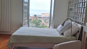 A bedroom with a bed, a chair, and a view of the city through large windows. - Spacious 3P in quiet palace, sea view in Menton (Menton)