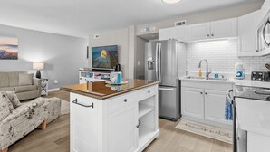 A modern kitchen with white cabinets, a built-in oven, and a stainless steel refrigerator. - Ocean Greens Unit E201 (North Myrtle Beach)