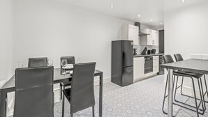 A modern kitchen with white cabinets, a black refrigerator, and a dining area with a table and chairs.