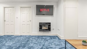 A room with a fireplace, a TV mounted above it, and a blue carpet.
