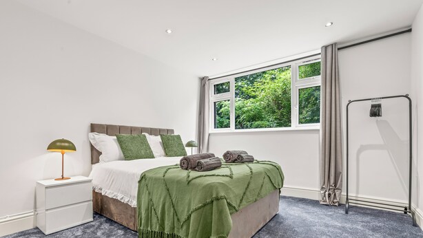 A bedroom with a bed, a nightstand, a window with curtains, and a radiator.