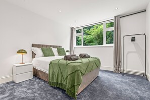 A bedroom with a bed, a nightstand, a window with curtains, and a radiator.