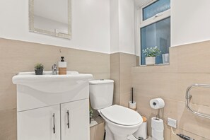 A modern bathroom with a white sink, toilet, and vanity. There is a window with potted plants on the windowsill.