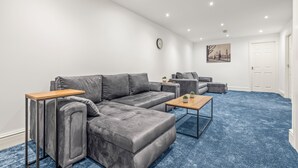 A modern living room with a grey sectional sofa, a wooden coffee table, and a blue carpet.