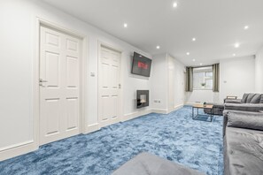 A modern living room with a blue carpet, a fireplace, a grey sofa, and a TV mounted on the wall.