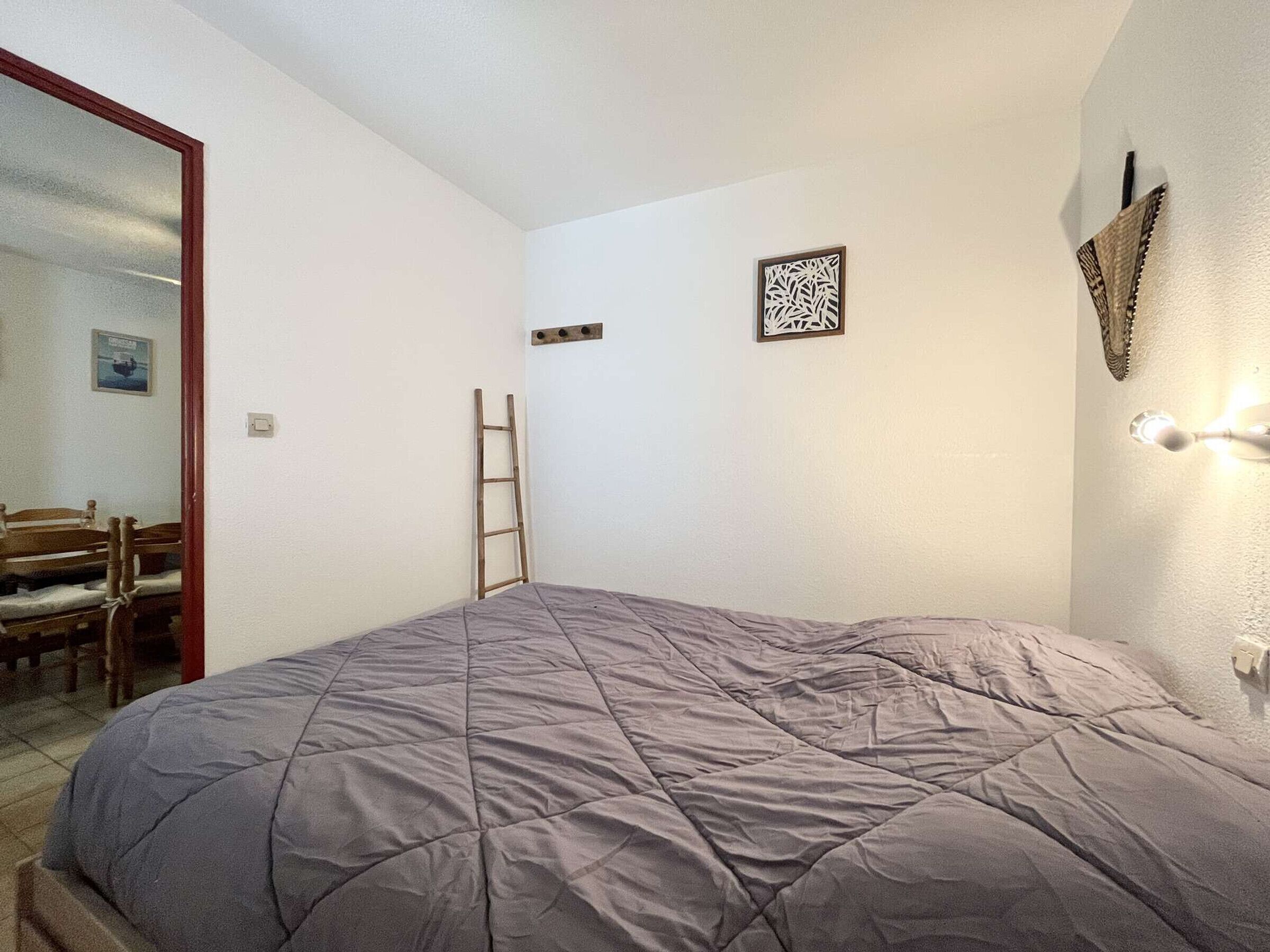 A bedroom with a bed, a ladder, a chair, and a wall-mounted light fixture.