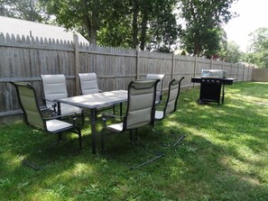 An outdoor patio with a dining table and chairs, a grill, and a wooden fence. - Cozy Cape Home Near Main St & Beaches (Barnstable)