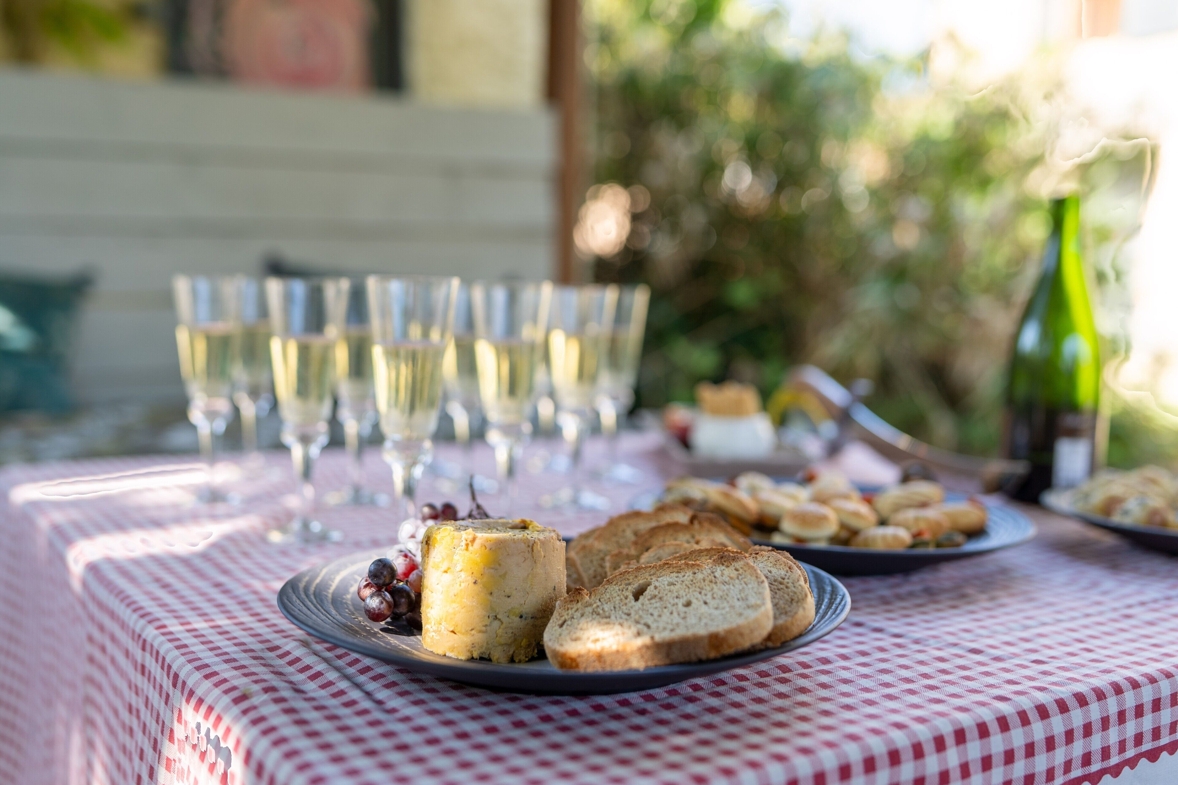 Une table recouverte d’une nappe à carreaux, avec des assiettes remplies de nourriture, des verres et une bouteille.