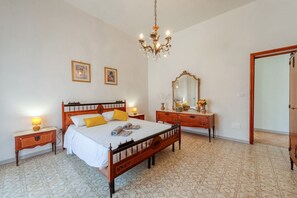 Quarto com cama de madeira, mesas de cabeceira, um espelho e um lustre.