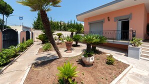 Zona residencial con una casa que tiene balcón, entrada para vehículos y un jardín con diversas plantas.