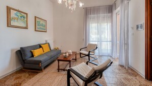Una sala de estar con sofá, sillón, mesa de centro, candelabro y obras de arte en las paredes.