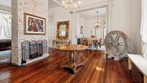 A room with a round wooden table, a fireplace, a large mirror, and a chandelier. - Bright Villa w Heated Pool & Pool Table 5br 4ba (New Orleans)
