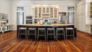 A spacious kitchen with a large island, wooden flooring, white cabinetry, and bar stools. - Bright Villa w Heated Pool & Pool Table 5br 4ba (New Orleans)