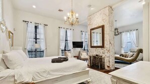 A bedroom with a large bed, a fireplace, a television, and a chandelier. - Bright Villa w Heated Pool & Pool Table 5br 4ba (New Orleans)