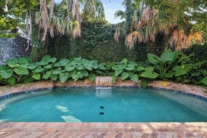 A swimming pool with a brick border, surrounded by lush greenery and a brick wall. - Bright Villa w Heated Pool & Pool Table 5br 4ba (New Orleans)