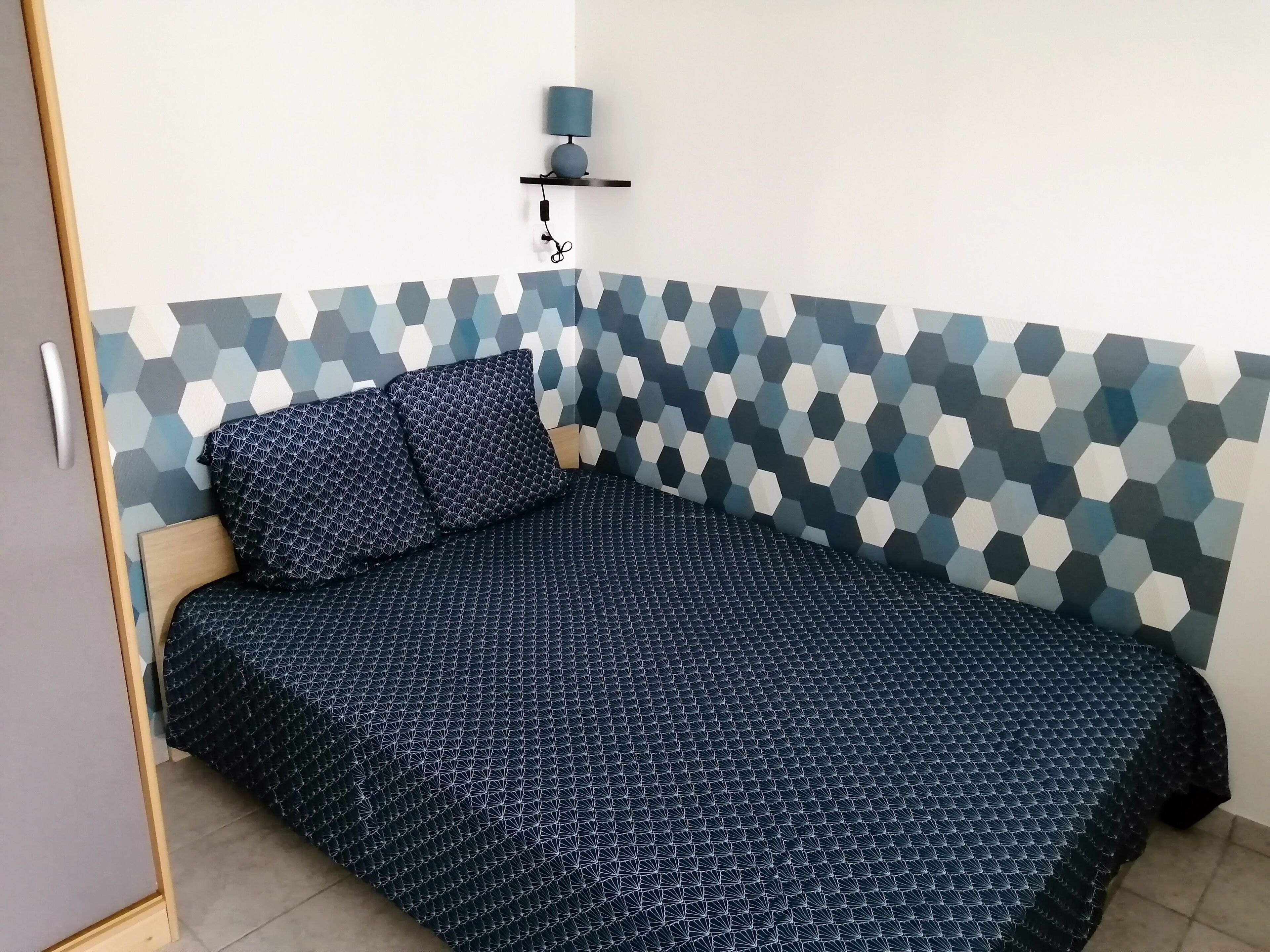 A bedroom with a geometric-patterned headboard, a bed with a matching geometric-patterned bedspread, and a wall-mounted lamp.
