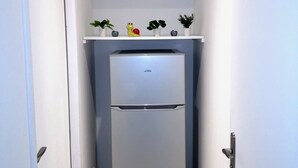 Une cuisine de taille réduite avec un réfrigérateur blanc, une étagère au-dessus contenant divers objets et une porte sur le côté gauche.