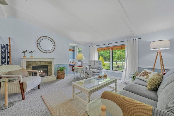 A living room with a fireplace, a sofa, a coffee table, and a view of the outdoors.