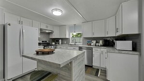 A modern kitchen with white cabinets, a central island, a stove, and a microwave. - Sunny 3BR w/ Firepit + Game Yard | Walk to Green Lake (Interlochen)