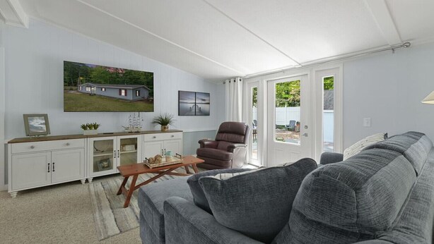 A living room with a grey sofa, a brown leather chair, a wooden coffee table, and a TV on the wall. - Sunny 3BR w/ Firepit + Game Yard | Walk to Green Lake (Interlochen)