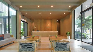 Una zona reception di un hotel con una scrivania in legno, due poltrone in vimini, un divano e piante in vaso.